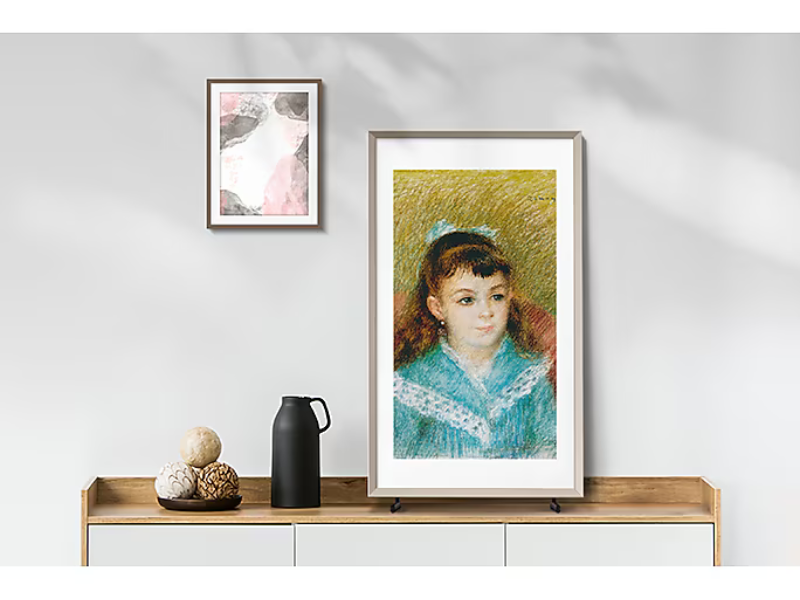 Samsung The Frame 32 Zoll FullHD QLED-TV steht auf einem modernen Sideboard, dekoriert mit einer schwarzen Vase, Deko-Kugeln und einem abstrakten Kunstbild an der Wand; ideal zum Mieten für stilvolles Wohnen oder Events.