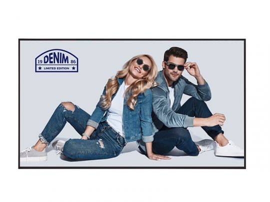 Zwei Personen tragen trendige Denim-Outfits und Sonnenbrillen. Eine Frau mit langen blonden Haaren sitzt neben einem Mann, beide wirken selbstbewusst. Sie trägt eine Denim-Jacke und zerrissene Jeans; der Mann einen kompletten Jeans-Look. Auf der Bildecke steht das Label "Denim Limited Edition 1986".