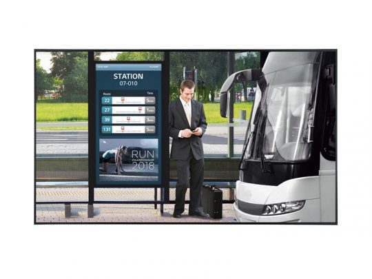 Ein Mann im Anzug steht an einer modernen Bushaltestelle, schaut auf sein Smartphone und hat einen Rollkoffer neben sich. Im Hintergrund ist ein Bus geparkt, während eine digitale Anzeigetafel Buslinien, Abfahrtszeiten und eine Veranstaltungswerbung zeigt. Die Szene vermittelt komfortables, zeitgemäßes Reisen mit öffentlichen Verkehrsmitteln.