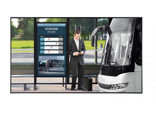 Ein Mann im Anzug steht mit einem Koffer an einer Bushaltestelle und schaut auf sein Smartphone. Neben ihm hält ein moderner weißer Bus. Die Bushaltestelle zeigt Fahrpläne und eine Werbung für eine Laufveranstaltung.