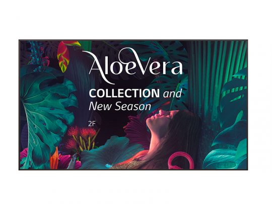 Eine Frau steht umgeben von leuchtenden grünen tropischen Blättern und blickt nach oben; im Vordergrund ist in großer weißer Schrift der Produktname "AloeVera COLLECTION" sowie "New Season 2F" zu sehen. Das Bild vermittelt Frische und Naturverbundenheit und bewirbt die neue AloeVera-Pflegeserie.